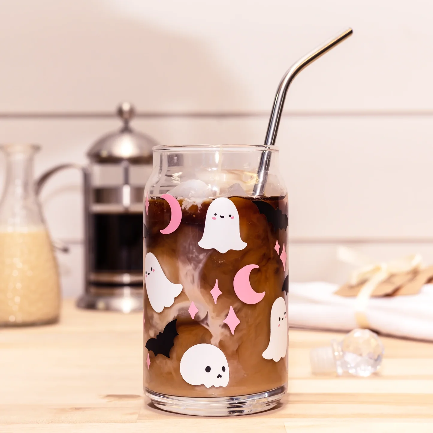 Glass of iced coffee with cartoon ghost and moon design on a kitchen counter.