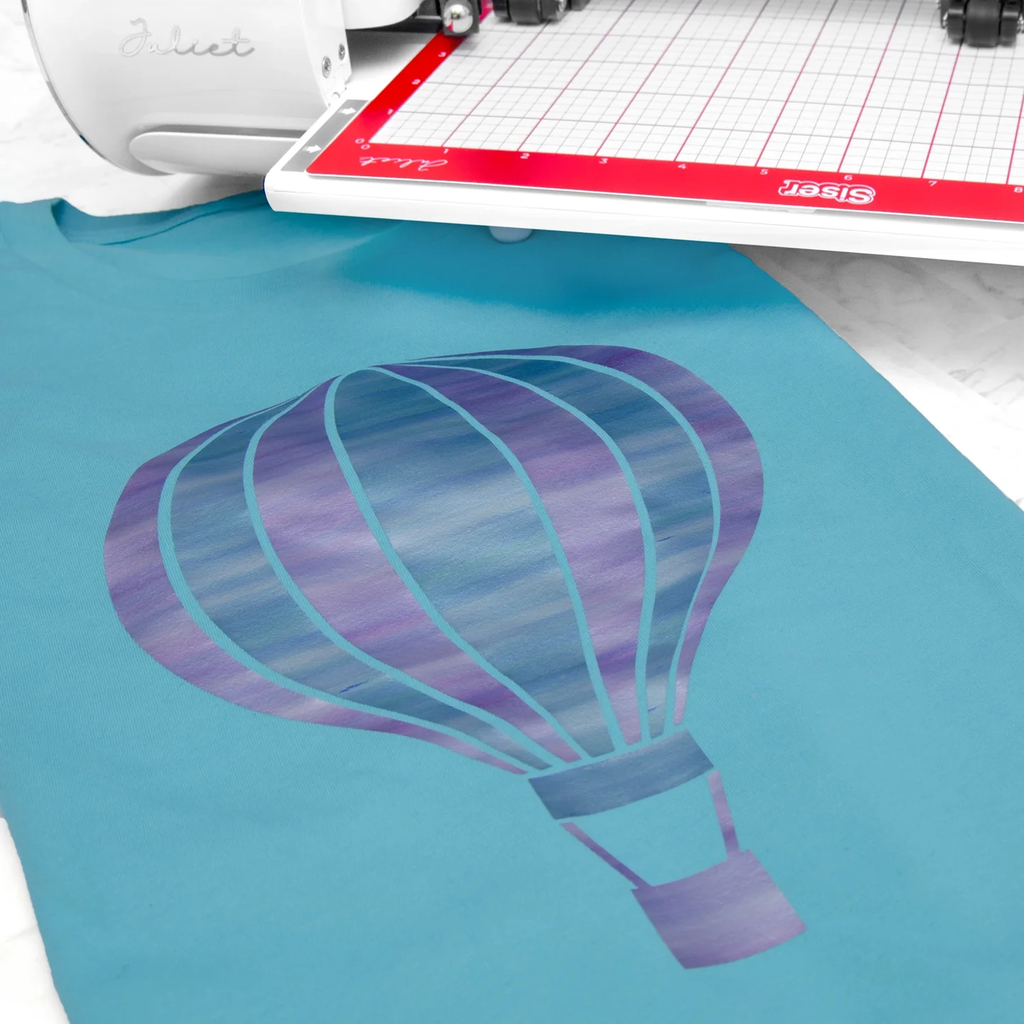 Cricut machine with a teal material featuring a purple hot air balloon design.