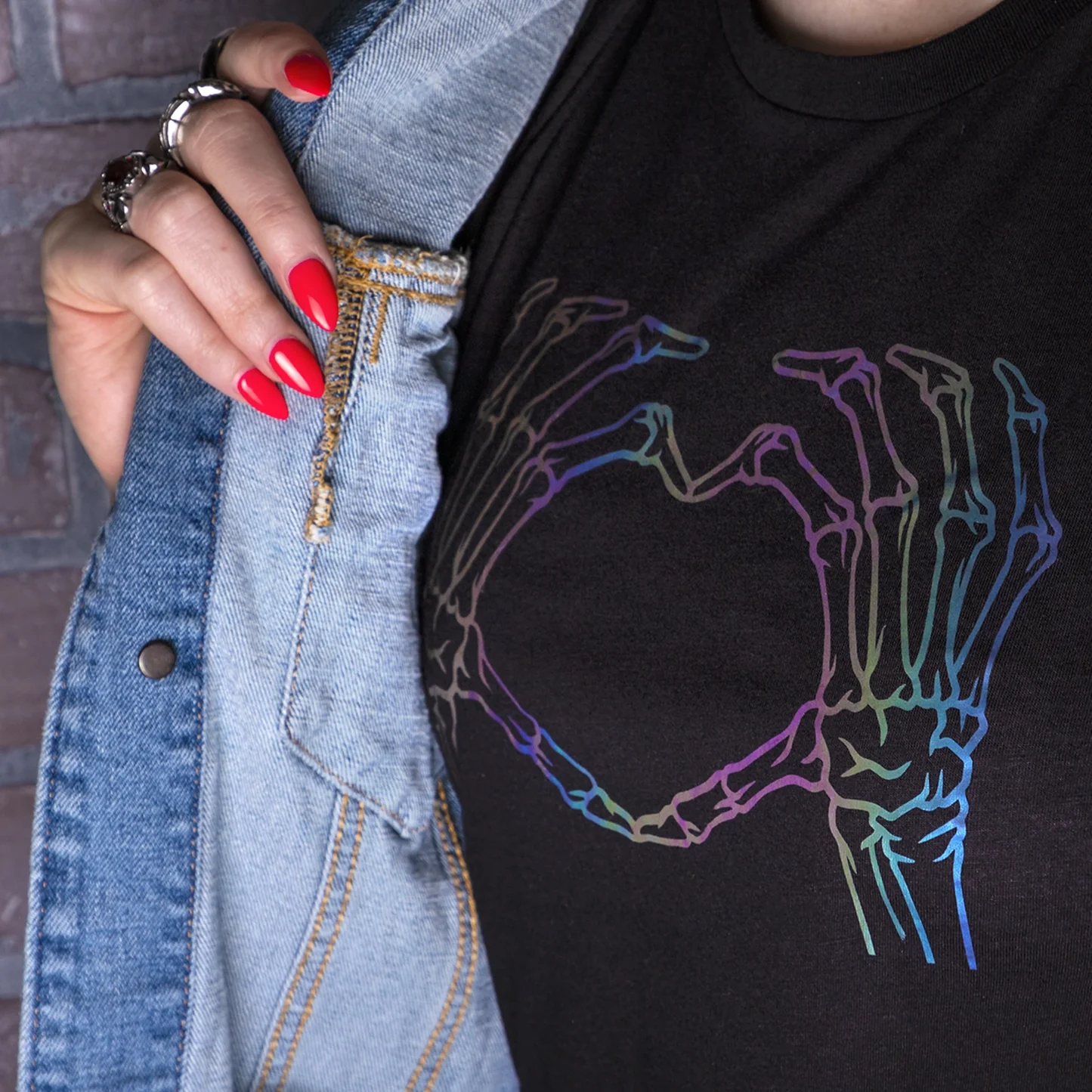 Person wearing a black t-shirt with a colorful skeleton hand design, holding a denim jacket.