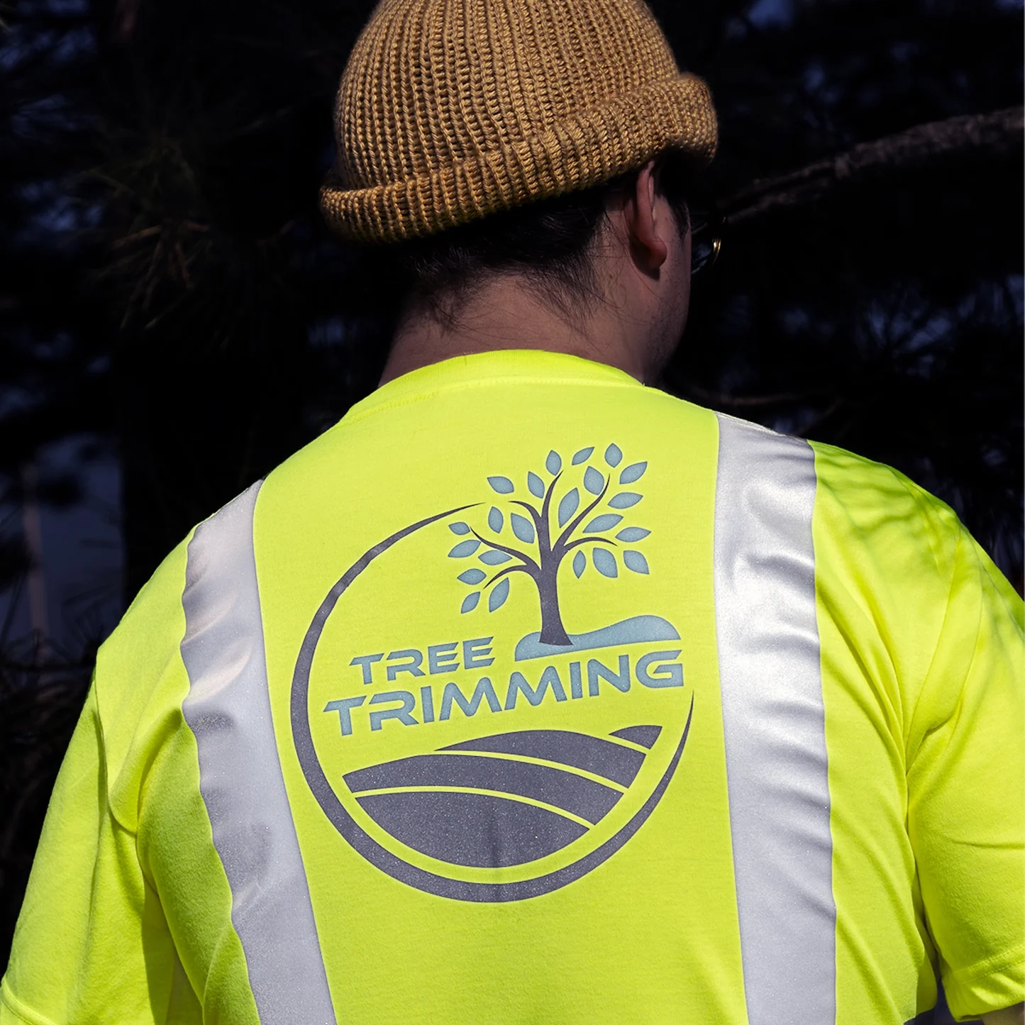 Person wearing a bright yellow 'Tree Trimming' safety vest with a tree graphic.