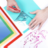 Hands using a tool to cut out a design from colored vinyl with a completed artwork in the corner.