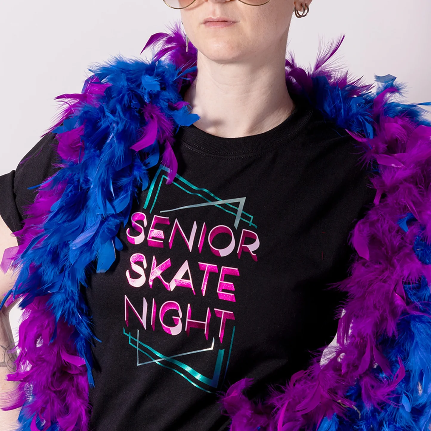 Person wearing a black t-shirt with 'Senior Skate Night' text and colorful feather boa.