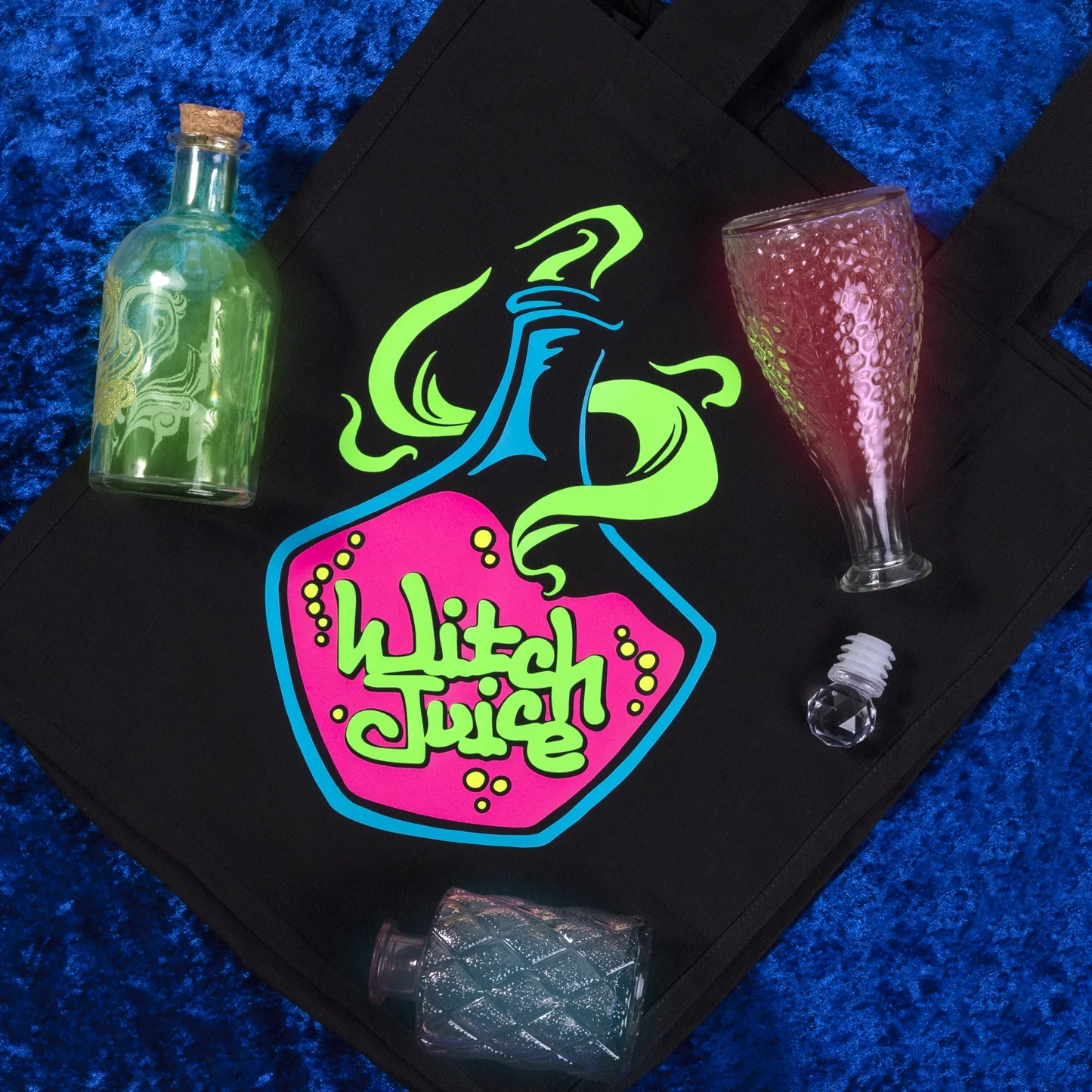 Black tray with 'Witch Juice' design, bottle, glass, and ice cubes on a blue textured surface
