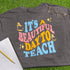 Gray t-shirt with colorful text 'It's a Beautiful Day to Teach' on grass with glasses and notebook.