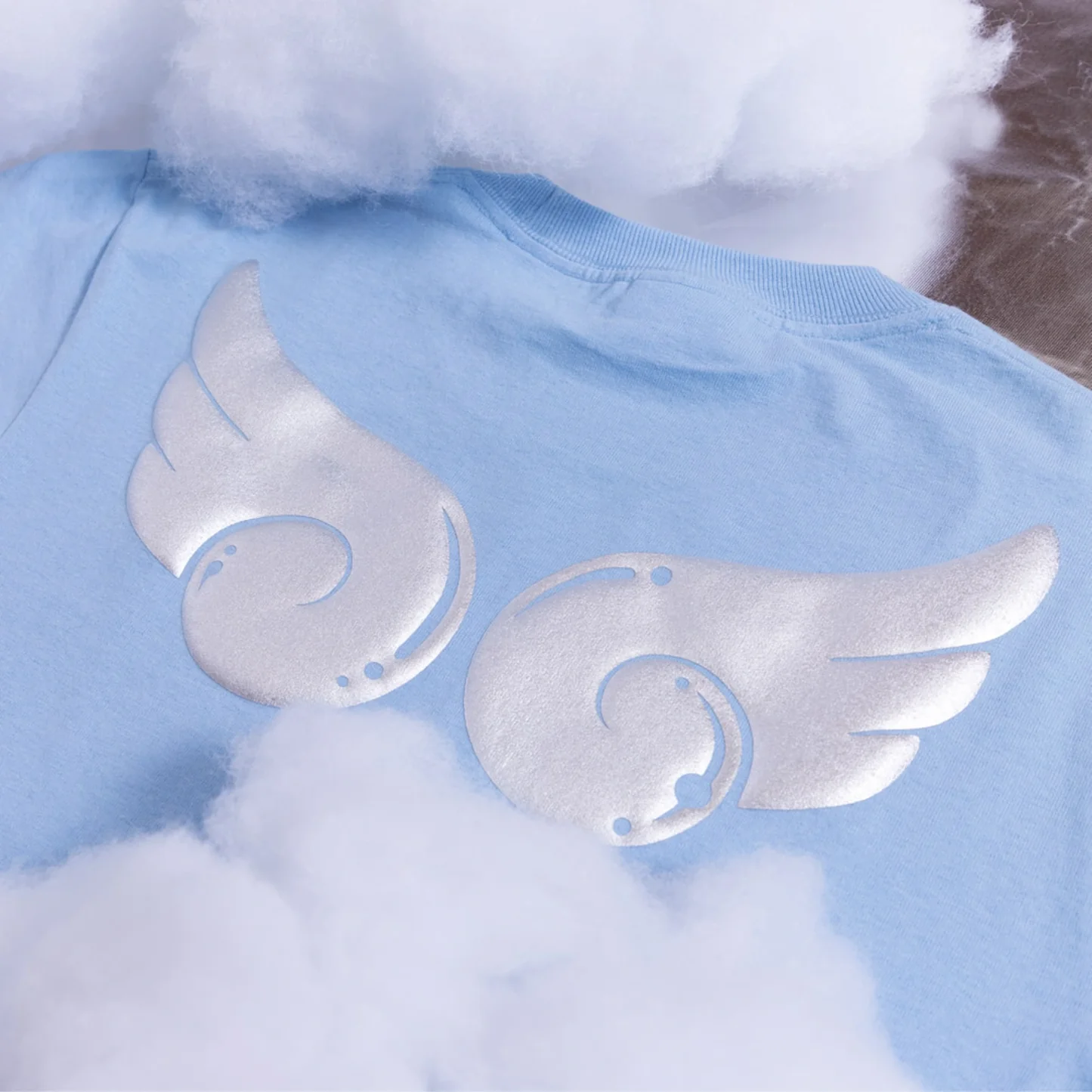 Light blue baby outfit with silver angel wings on a cloud background