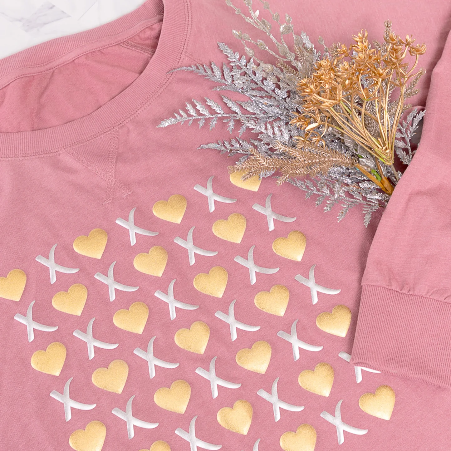 Pink sweatshirt with gold and white pattern, featuring a bouquet of dried flowers on a white background.