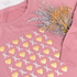 Pink sweatshirt with gold and white pattern, featuring a bouquet of dried flowers on a white background.