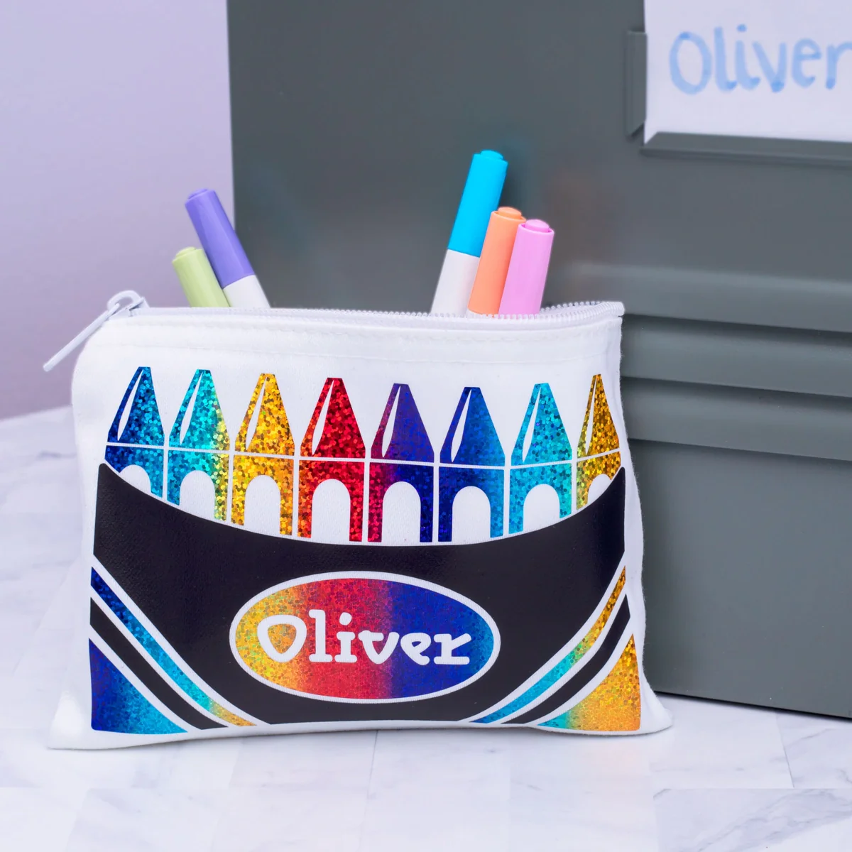 Pencil case with colorful crayon design and 'Oliver' text, containing markers.