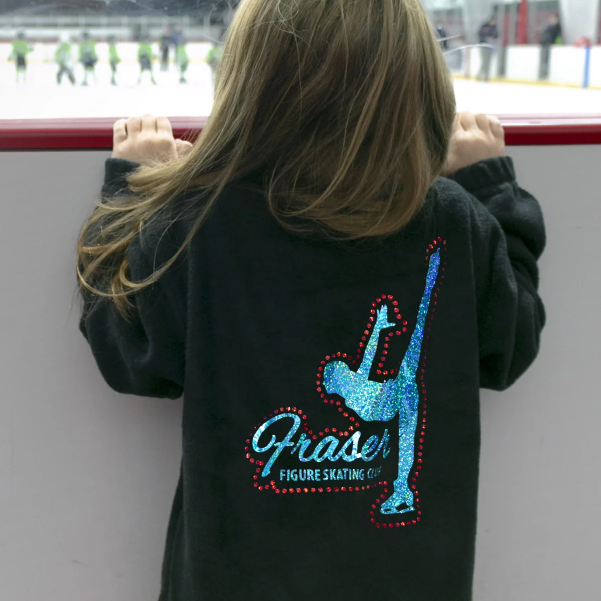 Person wearing a black hoodie with a blue figure skating design and 'Fraser Figure Skating Club' text, standing on an ice rink.