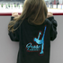 Person wearing a black hoodie with a blue figure skating design and 'Fraser Figure Skating Club' text, standing on an ice rink.