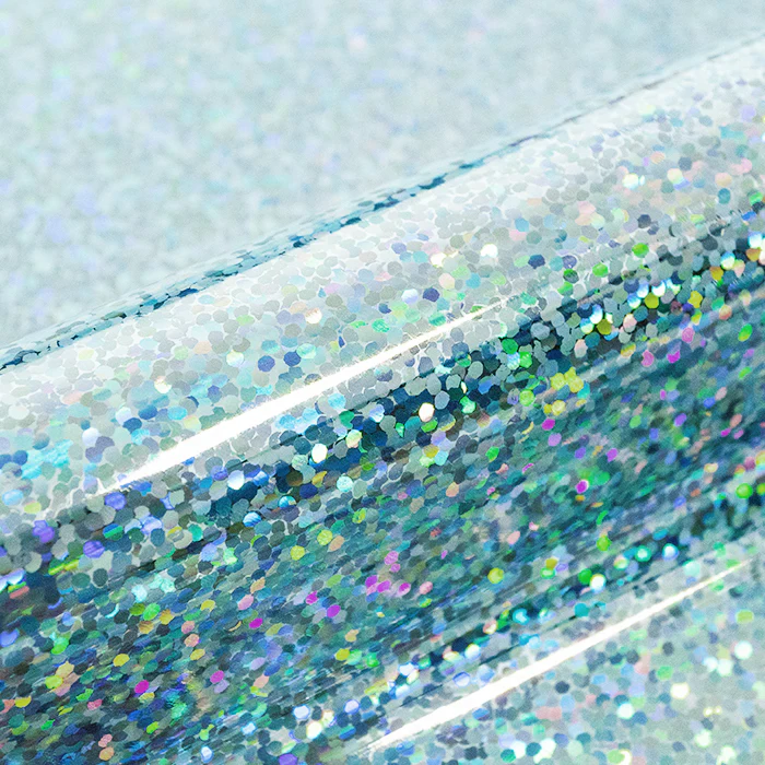 Close-up of a roll of glittery vinyl with multicolored sequins on a light blue background.