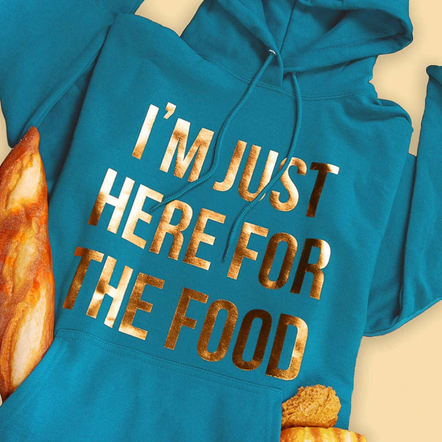 Blue hoodie with gold text 'I'm just here for the food' on a beige background