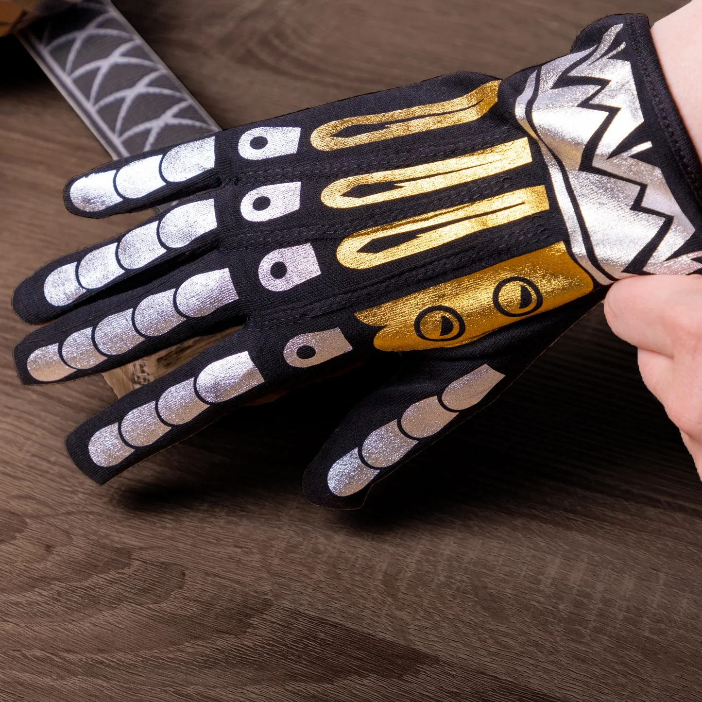 Gloves with black, gold, and silver design on a wooden surface