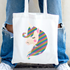 Tote bag with a colorful unicorn design held by a person wearing blue jeans and white sneakers.