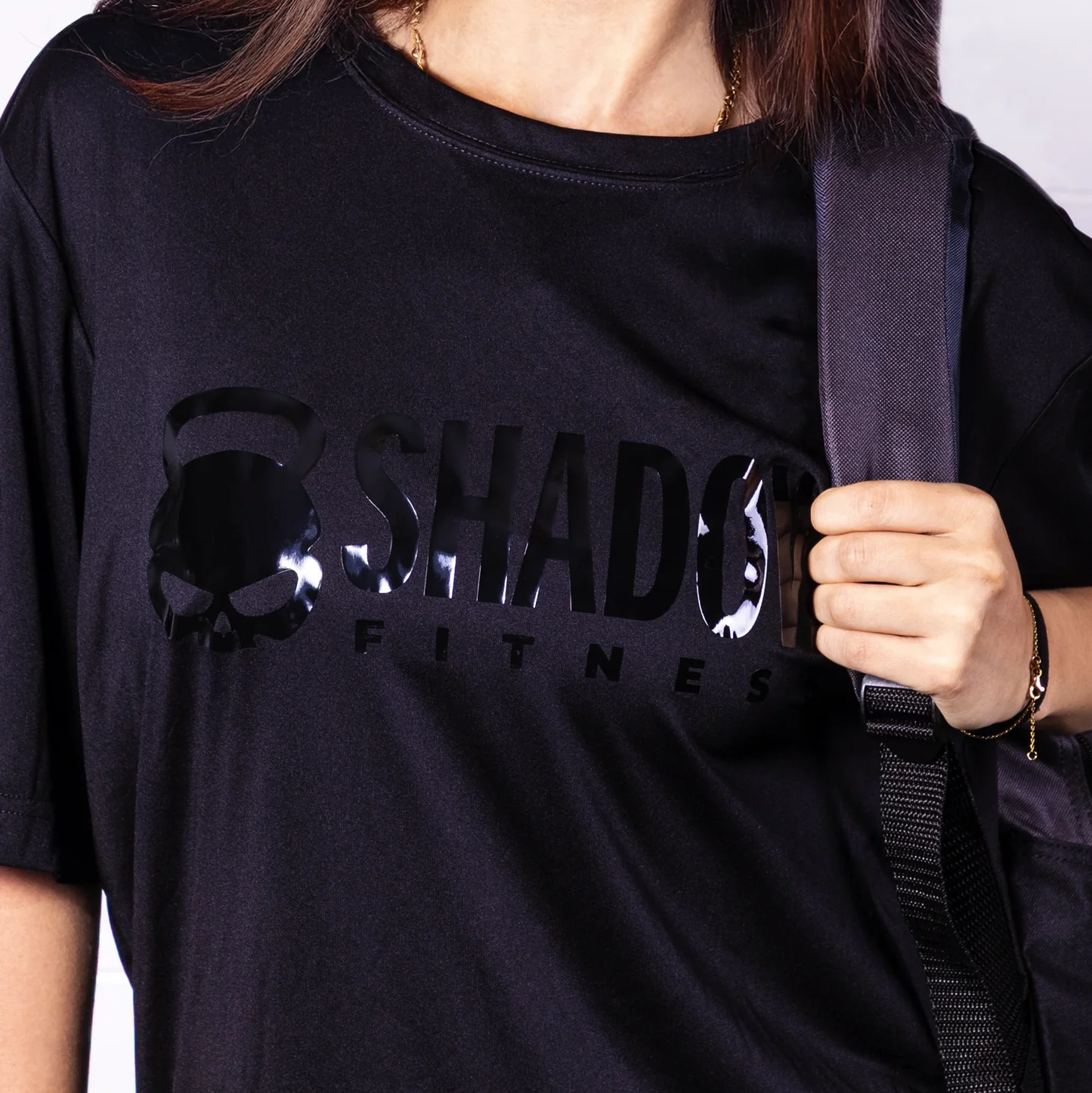Person wearing a black 'Shadow Fitness' t-shirt with a strap over their shoulder.