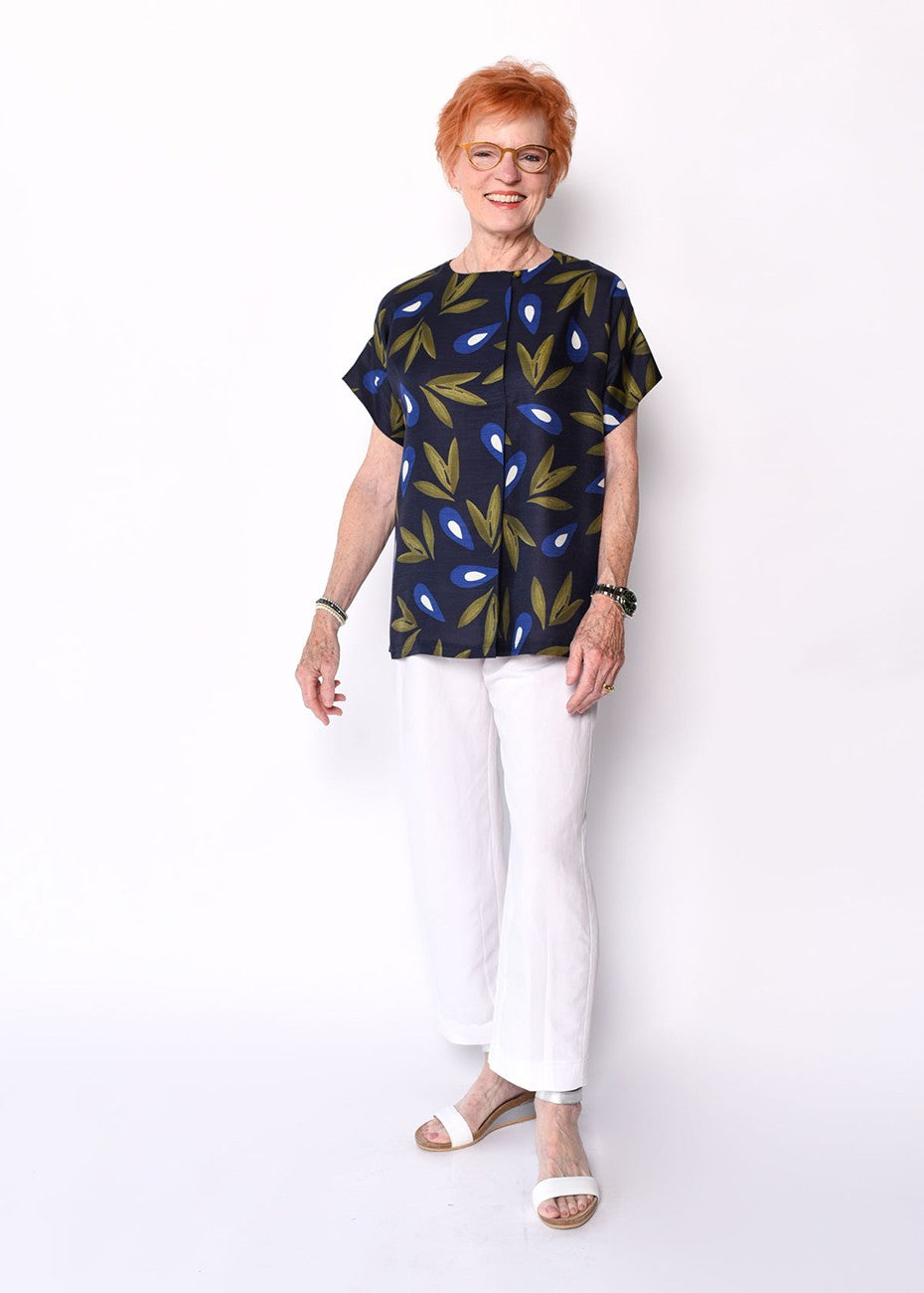 Woman wearing a patterned top and white pants against a white background
