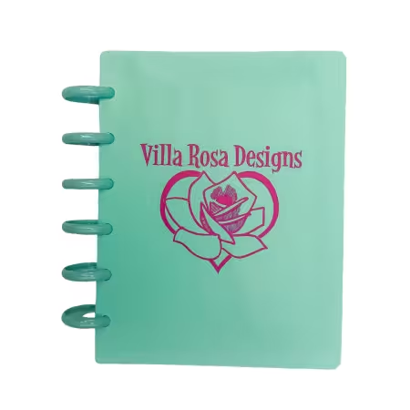 A mint green spiral-bound notebook with a pink rose graphic and the text 'Villa Rosa Designs' printed on the cover, shown against a plain white background.