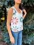 Woman wearing a sleeveless floral top and jeans standing in front of greenery