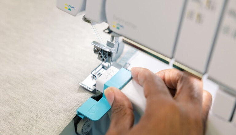 A close-up of a person's hands guiding a light blue fabric under a white and gray industrial sewing machine.