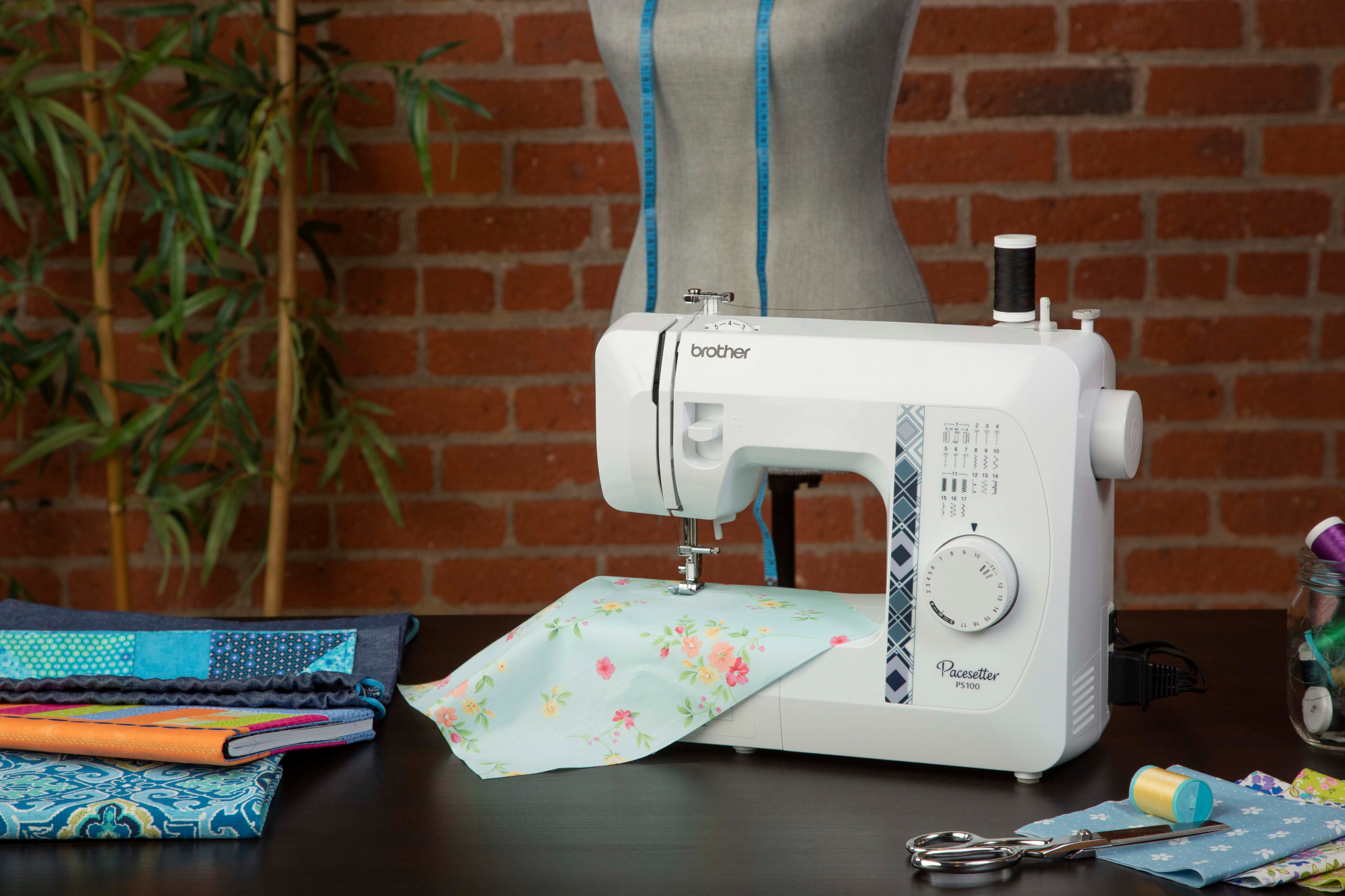 image of the Brother Pacesetter PS100 Sewing and Quilting Machine on a table with a sewing example and sewing supplies