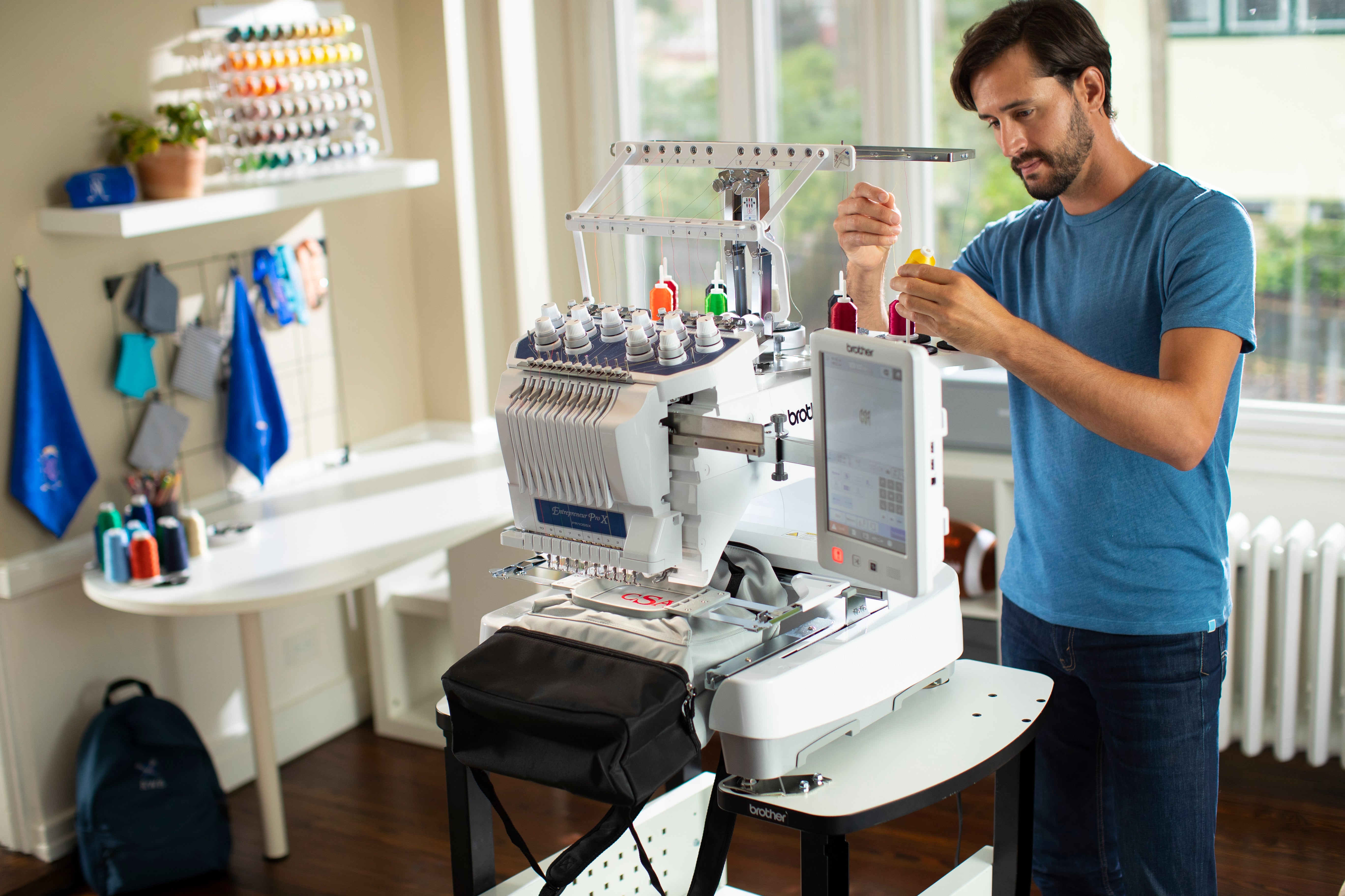 Image of a man threading the Brother EntrepreneurPro X PR1055X fourteen by eight ten needle embroidery machine in a room with sewing equipment