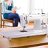 image of the Brother RPQ1500SL Sewing Machine on a table with a woman in the background
