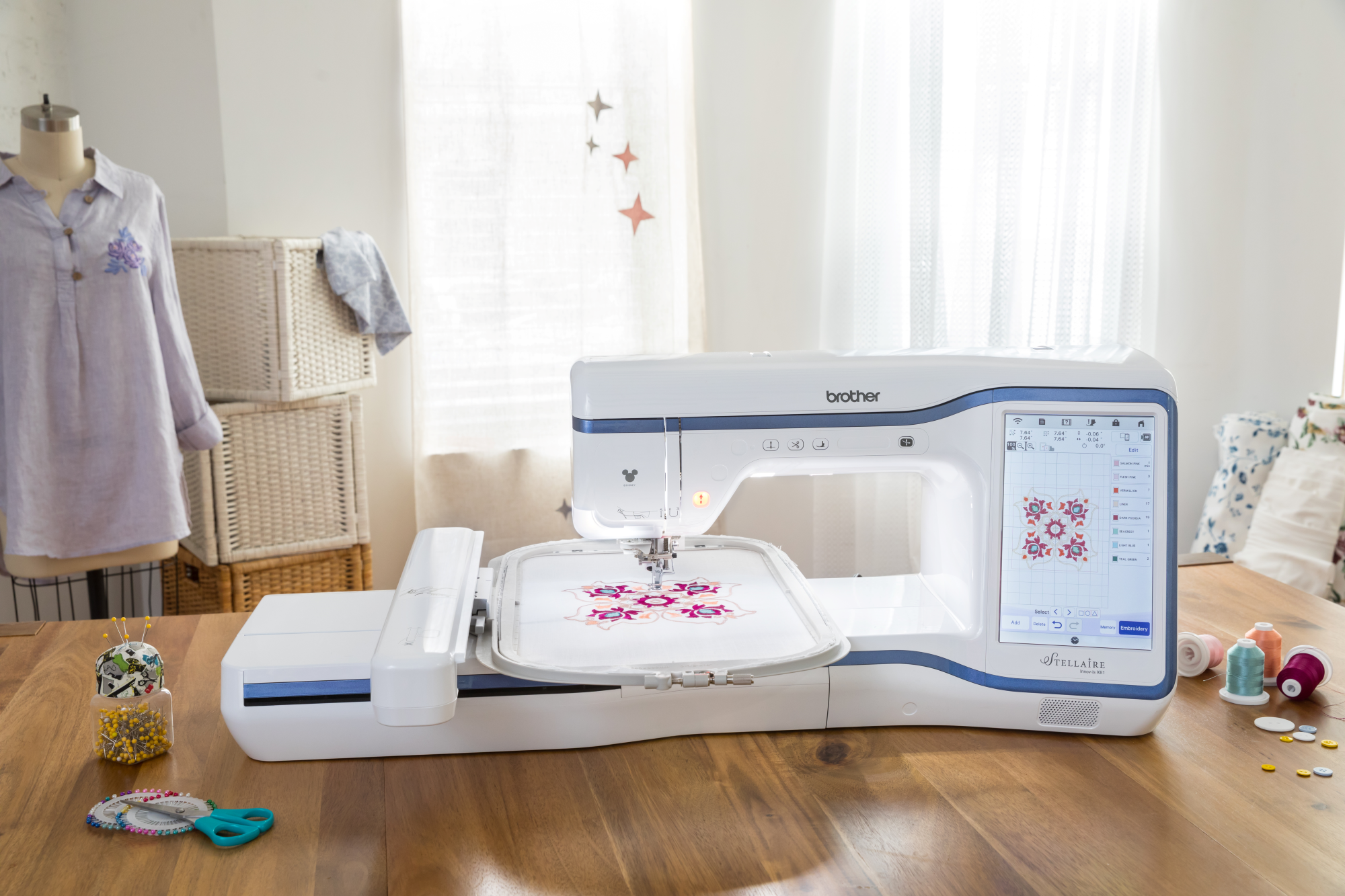image of the Brother Stellaire Innov-is XE1 fourteen by nine and a half Embroidery Machine with example embroidery on a talbe with sewing supplies