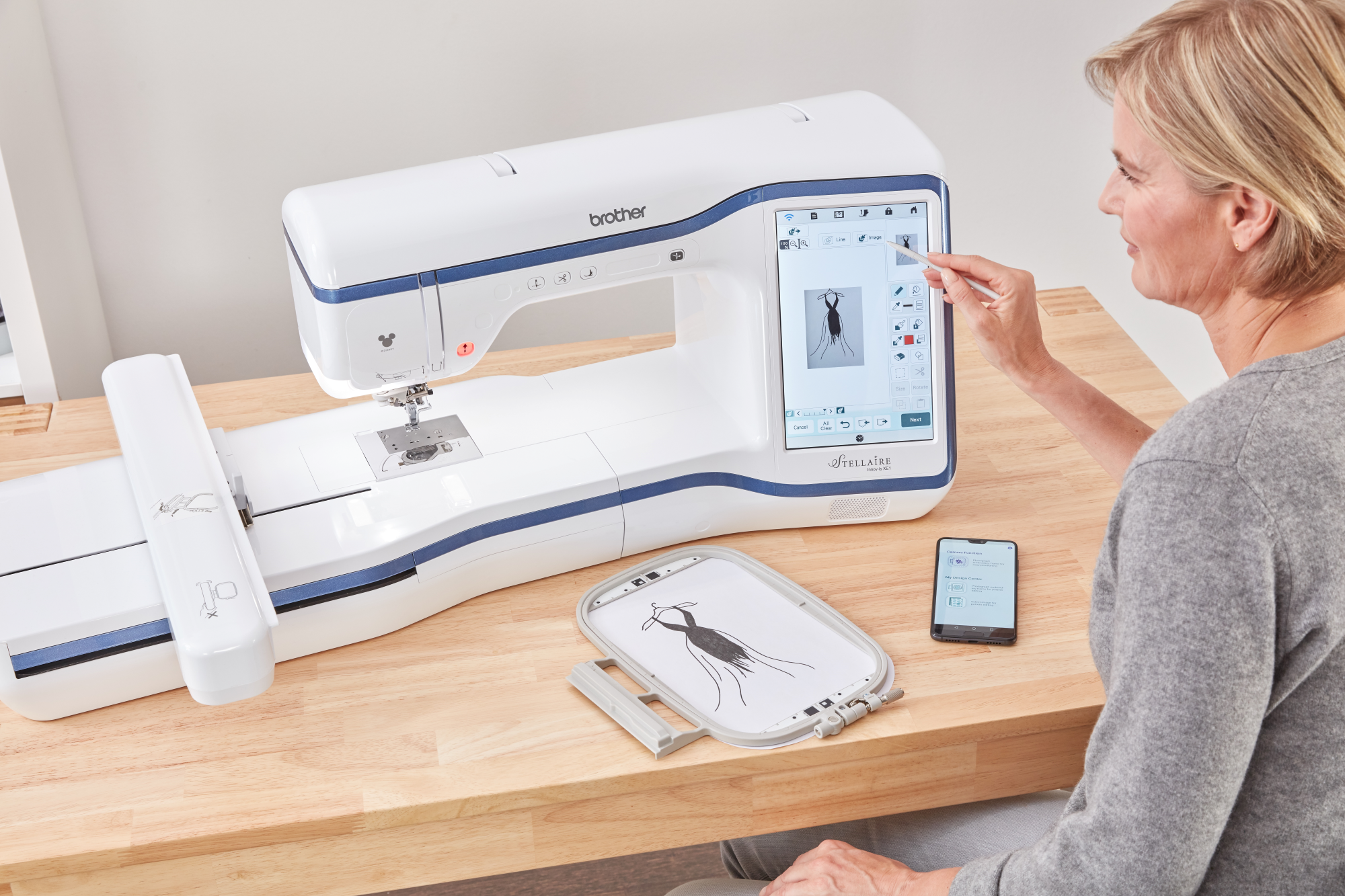 image of a woman using the Brother Stellaire Innov-is XE1 fourteen by nine and a half Embroidery Machine and the My Design Snap Mobile App to create a design