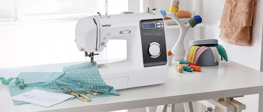 image of the Brother ST150HD Strong and Tough Computerized Sewing Machine on a table with sewing supplies and sewing example
